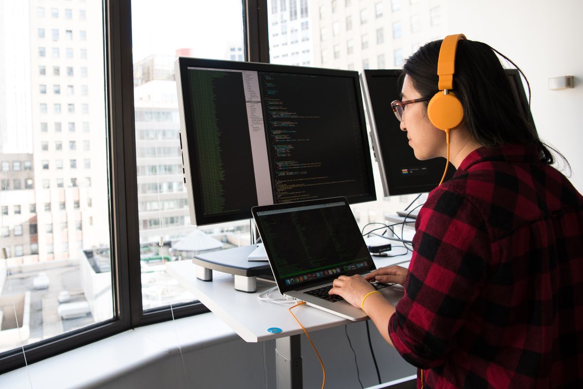 African woman developer programming on laptop at standing desk in modern office